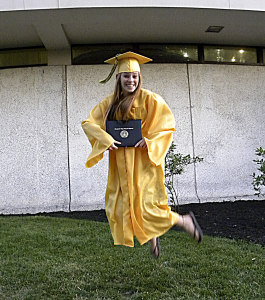 счастливая выпускница в желтой мантии прыгает с дипломом в руках